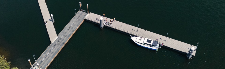 Luchtfoto van een aanlegsteiger met een aangemeerde boot en mensen die genieten van de zon aan het water.