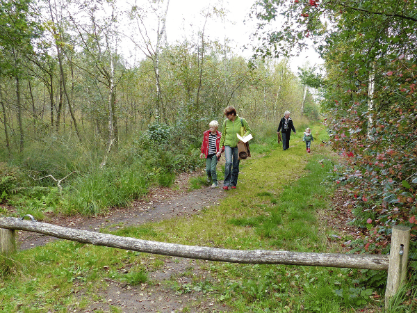 Kind loopt samen met een vrouw over een bospad. Een stukje achter hun loopt nog een vrouw met een wat jonger kind