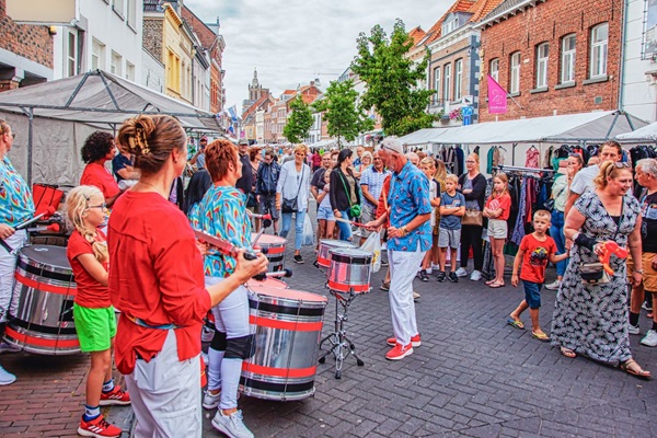Perkussionsvorstellung auf dem Sjoemelmert in Roermond, mit Musikern in farbenfroher Kleidung und einer begeisterten Menge zwischen den Marktständen.