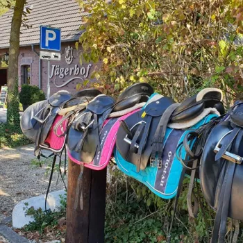 Zadelrekken met kleurrijke zadels bij een manege of paardenhotel in Limburg, met op de achtergrond het gebouw van Jägerhof en een parkeerbord voor ruiters.