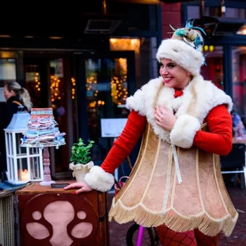 Straatartiest in feestelijke lampenkapoutfit tijdens winteractiviteit in een sfeervol verlichte straat in het centrum van Weert.