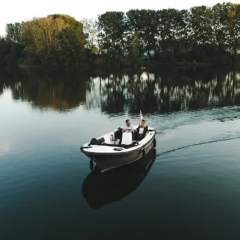 Twee personen varen in een motorboot over de Maasplassen, met rustig water en bomen langs de oever.